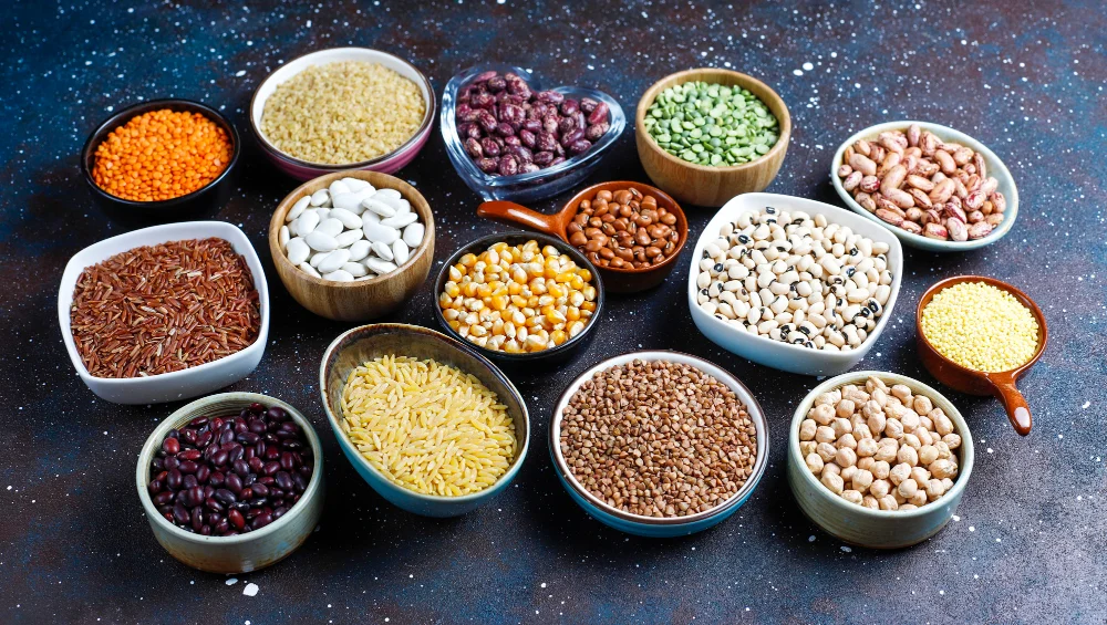 Dažādi augu valsts olbaltumvielu avoti – pupiņas, zirņi, lēcas, griķi un citi pākšaugi bļodiņās uz tumša fona