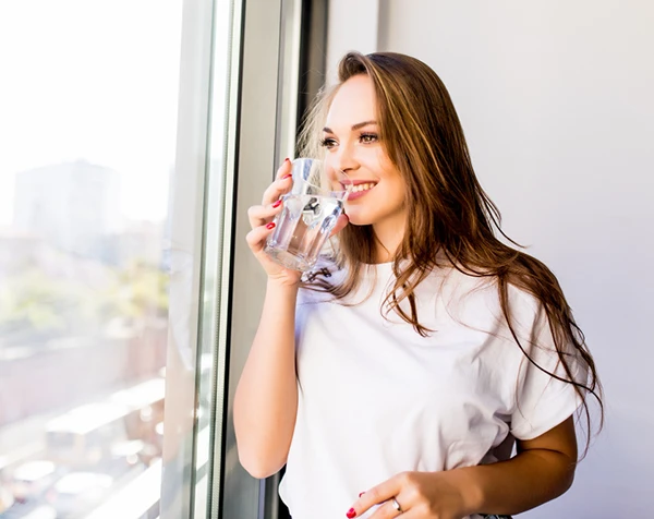 Sieviete smaida un dzer siltu ūdens glāzi no rīta – veselīgs dzīvesveids