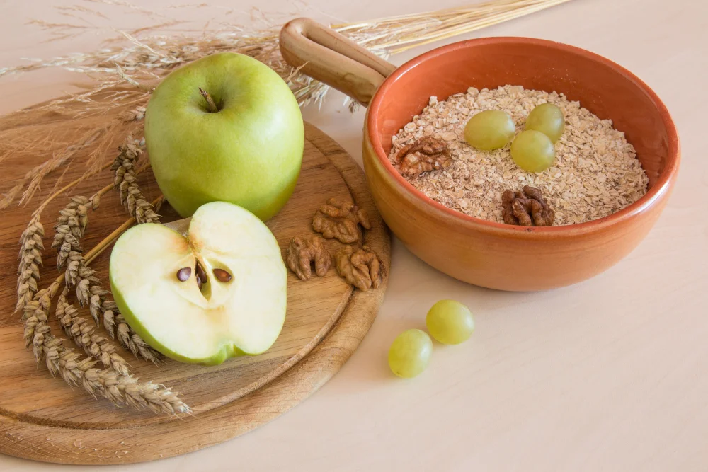 Šķiedrvielām bagāti produkti: ābols, auzu pārslas, rieksti un vīnogas uz galda