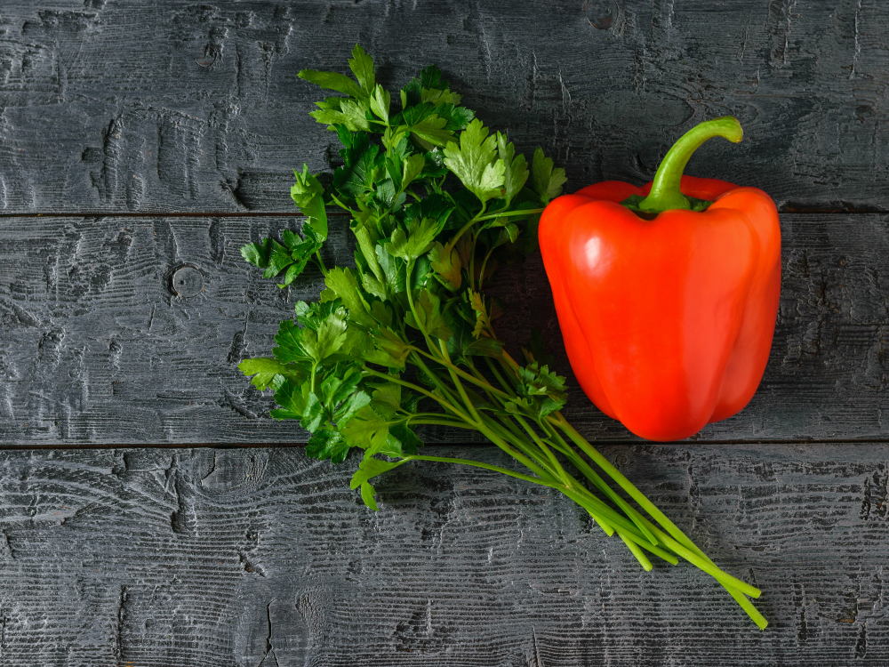Karotinoīdi – sarkana paprika un pētersīļi uz tumša koka galda