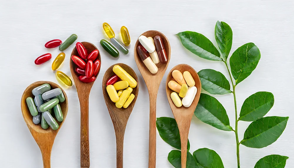 Vitamīnu kapsulas un tabletes koka karotēs ar zaļām lapām uz balta fona