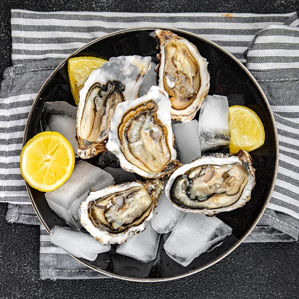 Svaigas austeres uz ledus ar citronu šķēlītēm melnā šķīvī