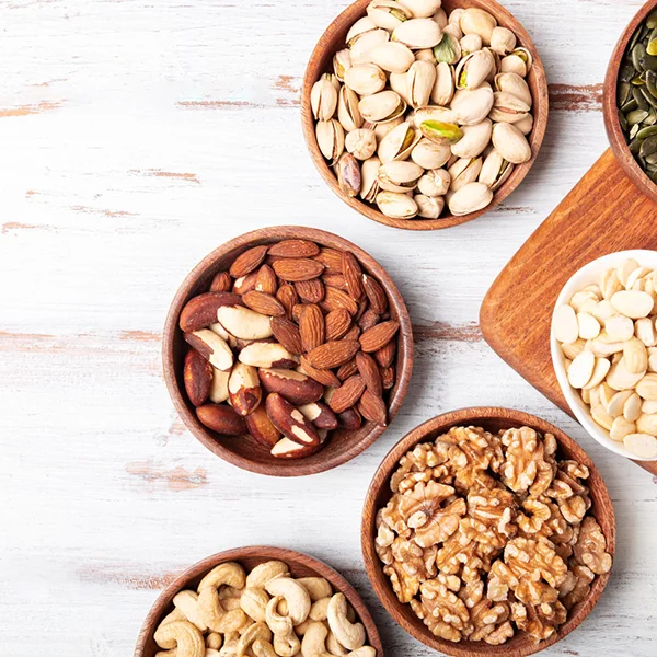 Dažādi rieksti un sēklas koka bļodiņās uz gaiša koka virsmas